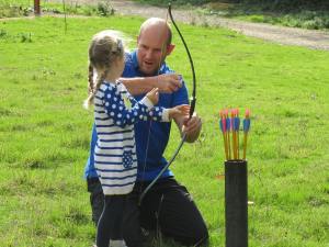 man helping girl do archery